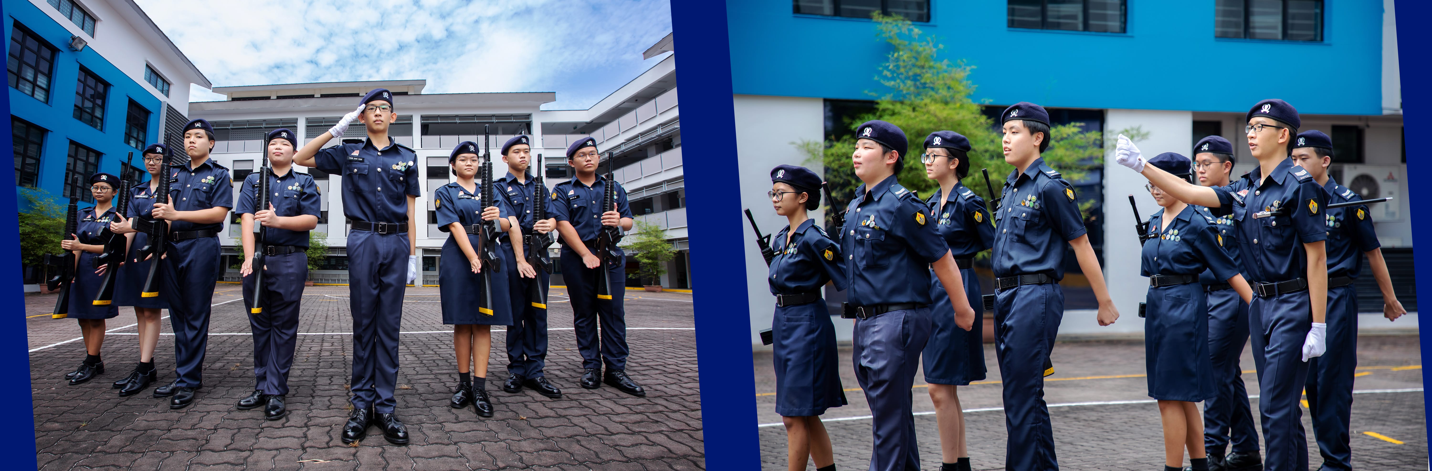 Youth cadets in navy uniforms and berets stand at attention and practice drills with rifles in a school courtyard.